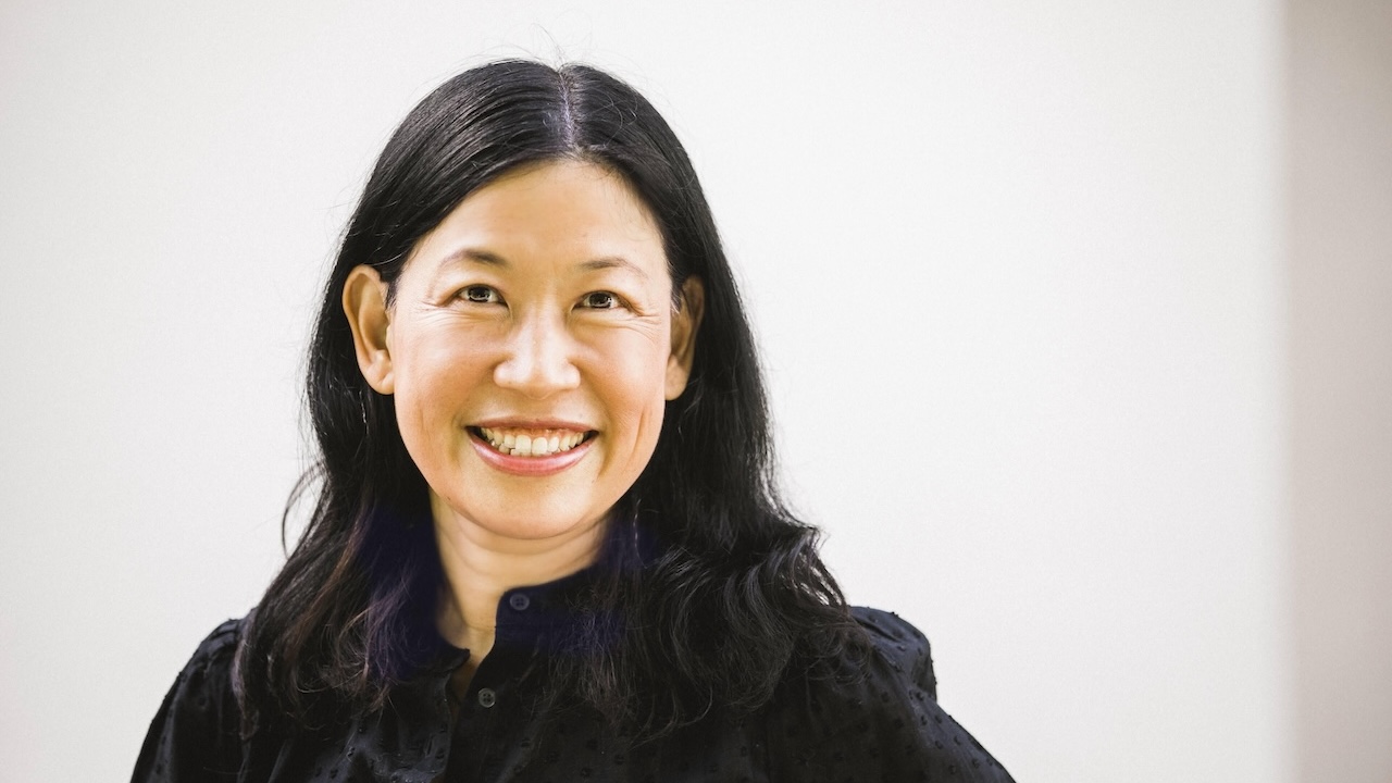Headshot of smiling middle aged woman with shoulder length black hair and button up shirt against white background.